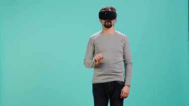 Sanal gerçeklik kulaklığı takan, arayüzle etkileşim kuran, hareketler yapan bir adam. İleri teknoloji modern VR cihazını kullanarak eğlenen kişi mavi stüdyo arka planında izole edilmiş, kamera A