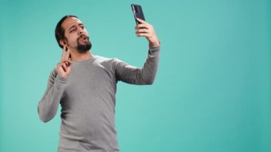 Akıllı telefonu kullanarak selfie çeken ve sosyal medyaya, stüdyo arkaplanına koyan bir adam. Fotograf makinesiyle fotoğraf çeken kibirli biri, stüdyo arka planında izole edilmiş, kamera B