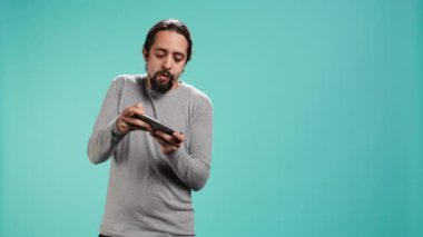 Odaklanmış adam cep telefonuyla yoğun video oyunu oynuyor, dokunmatik ekrandaki saldırı tuşlarını spamlıyor. Oyuncu oyun yarışmasına katılıyor, stüdyo arka planında izole edilmiş, kamera B