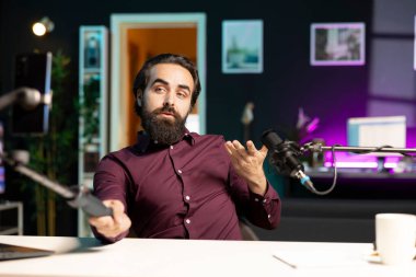 İçerik yaratıcısı cep telefonuyla konuşuyor stüdyoda selfie çubuğuna bağlı, mikrofon kullanarak izleyicilerle sohbet ediyor. Vlog kaydetmek için telefon kamerası ve profesyonel mikrofon kullanan bir adam