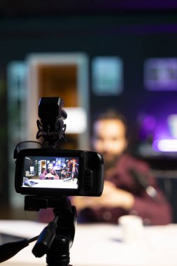 Bulanık arka plan sunucusunda içerik yaratıcısı tarafından kullanılan profesyonel kameraya odaklanın. Neon lit stüdyosunda çevrimiçi program sunuyor. Vlogger 'ın yayın sırasında kullandığı yüksek teknoloji ekipmanlarını kapat