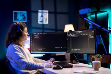 Yazılım kalitesi güvencesi verirken müzik dinleyen, kaynak kodları bilgisayar ekranında okuyan bir kadın. Kulaklık takan yönetici, podcastların keyfini çıkarıyor ve masaüstü bilgisayarındaki kodlamayı denetliyor