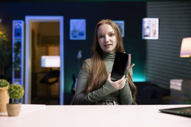 Gen Z internet şovu sunucusu yılın en iyi cep telefonu sürümleri hakkında içerik kaydediyor. Genç içerik yaratıcısı yeni başlatılan cep telefonu incelemesini daire stüdyosunda kaydediyor