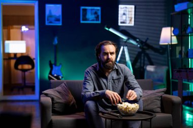 Tembel koltuk patatesi TV 'de televizyon izleyip patlamış mısır yiyor, çene düşürme eylemine kapılmış, ekrana dikkatle bakıyor. Düşüncesizce eğlenirken oturup abur cubur yiyen adam.