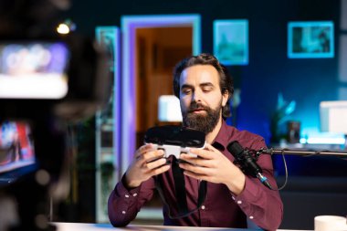 Seyircilere sanal gerçeklik gözlüğü sunan gülümseyen adam profesyonel kamerayla video çekiyor. İçerik yaratıcısı, hayranlarına önermeden önce sanal gerçeklik ürünü deniyor.