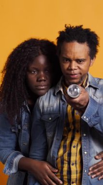 Dikey Afrikalı Amerikalı adam korkmuş karısını korumak için el fenerini kullanıyor. Korkan kadın sarı arka plandan korunmak için sevgilisinin arkasına saklanıyor. Korkmuş bir an. Kamera.