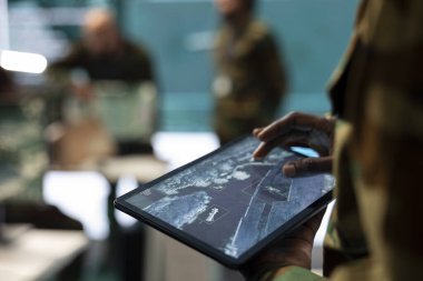 Tabletindeki konuşlandırılmış piyade birliğini uydu sistemi ve dünya haritası kullanarak analiz et. Bilgi işlem mühendisi keşif için yüksek teknoloji ekipmanlarıyla çalışıyor. Kapat..