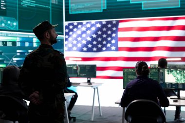 Yüksek teknoloji ofisindeki tehdit tespit faaliyetlerini denetleyen bir Amerikan askeri büyük ekrandaki çok gizli verileri inceliyor. Melez savaşı yöneten hükümet askerleri, siber saldırı önleme.