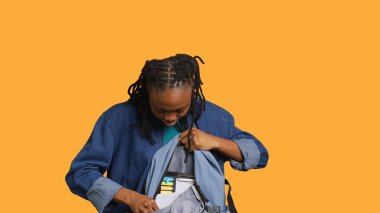 Sırt çantasını karıştıran neşeli bir kadının portresi, okul için finansal grafikler, stüdyo geçmişi. Parlak kız sırt çantasından birinci sınıf malzeme çıkarıyor.