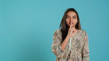 Annoyed indian woman doing shushing hand gesturing, irritated by noise, having negative mood. Person placing finger on lips, doing quiet sign gesture, isolated over studio background, camera A clipart