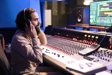 Ses mühendisi, kontrol odasında plaklarını dinlemek için kulaklık kullanıyor. Parçaları düğmeler ve motorlu faders ile karıştırıp ustalaştırıyor. Yetenekli teknisyen yeni bir albüm üzerinde çalışıyor..