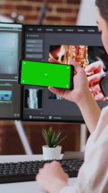 Yeşil ekranda serbest çalışmak için evden çalışan dikey video Asyalı kadın editör akıllı telefon ve video karıştırma yazılımı için çift monitör kullanıyor. Teknoloji araçlarıyla donatılmış yaratıcı çalışma alanı