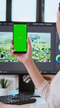 Modern bir ortamda yeşil ekranın yanında çalışan dikey Video Profesyoneli Asyalı kadın çift monitör ve gelişmiş video düzenleme yazılımı kullanıyor. Yapım sonrası çoklu görev