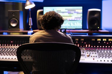 Ses teknisyenleri dijital yazılım arayüzü ile stüdyodaki kontrol odasında müzik düzenleme ve işleme parçalarını düzenliyor. Stereo teknik ekipmanlarla müzik yapan genç bir uzman.