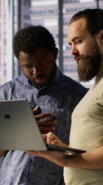 Ofisteki dikey video bilgi işlem çalışanları dizüstü bilgisayar, test ve konuşlandırma programları ve sistemleri kullanarak birlikte çalışıyorlar. Geliştirici ve meslektaşı defter üzerinde kod kontrol ediyor, çalışma alanında beyin fırtınası yapıyor.