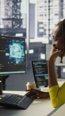 Ofisteki dikey video elemanı mesai sırasında esniyor, bilgisayardaki yapay zeka yazılımına bakarken yorgun hissediyor. Yorgun düşmüş Afro-Amerikan yapay zeka şirketi çalışanı