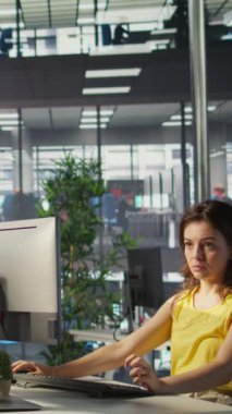 Dikey video işçisi iş vardiyası sırasında bilgisayar kullanarak ofis masasında oturuyor, online finansal iş belgelerine bakıyor. Çalışma alanında çalışan bir şirket çalışanı PC ile ilgili görevler yapıyor, verimli oluyor.