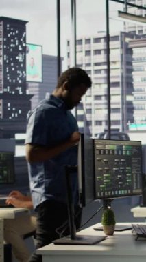 Dikey bilgisayar bilimcisi çalışma alanında gezindikten sonra PC kullanarak yazılım hata ayıklama işlemine devam ediyor. Ofiste tabletle yürüyen bir adam, kodlama sorunlarını bilgisayar, kamera B kullanarak düzeltiyor.