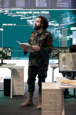 Askeri personel, askeri harekat üssündeki büyük ekranda canlı uydu görüntülerini inceliyor. Gelecekteki ulusal güvenlik görevleri için istihbarat topluyorlar. Görevli keşif sistemi çalıştırıyor..