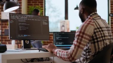 Afrika kökenli Amerikan bilişim uzmanları ofis içinde çift monitörlerde programlama kodları yazılımsal gelişim ve internet güvenliği üzerinde çalışıyorlar. Uzaktan çalışma ve verimlilik için ideal bir kurulum. Kamera B.