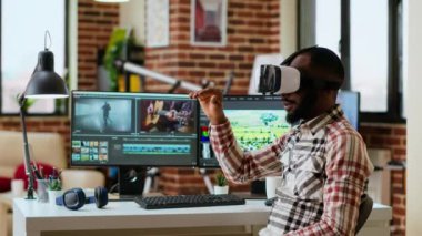 Afrikalı Amerikalı editör renk değerlendirmesi yapmak için sanal gerçeklik gözlüğü kullanıyor, yüksek teknoloji VR kulaklığı ve ev ofisindeki çift monitörlerle çalışıyor. Video kliplerini düzenleyen film yapımcısı. Kamera B.