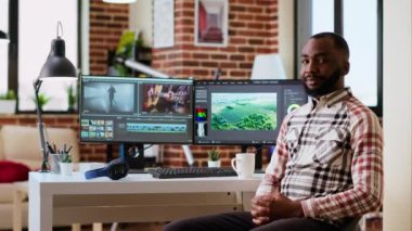 Afrikalı Amerikalı erkek film yapımcısı yaratıcı kurgu yazılımı, karıştırma ve renk derecelendirme video kliplerinde çalışıyor. Oturma odasında üretim araçları ve çift monitörler var. Kamera B.