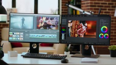 Oturma odasında boş bir masa var. İkili monitörlerde bir video projesi, video yapımı var. Ortam oluşturma için yazılım ve teknoloji araçları ile uzak çalışma için optimize ofis ayarları.