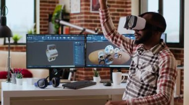 Erkek 3D mühendis çift monitörlerde yapay zeka ve profesyonel CAD yazılımı kullanarak VR kulaklıklı endüstriyel bir prototip geliştiriyor. Afrikalı Amerikalı serbest çalışan biri. Kamera B.