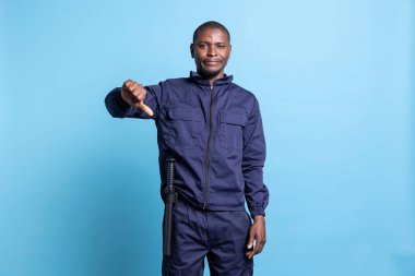 Güvenlik görevlisi, kameranın önünde fikir ayrılığını gösteren hoş olmayan davranışlar sergiliyor. Gardiyan bir şeyi reddederek otoritesini gösteriyor. Stüdyoda olumsuz bir sembol..