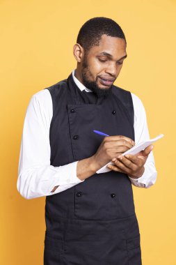 Yetenekli restoran sunucusu müşterilerinden yemek siparişini defterine alır ve müşteri memnuniyeti için yiyecek ve içecek seçimini yazar. Stüdyoda önlüklü profesyonel garson..