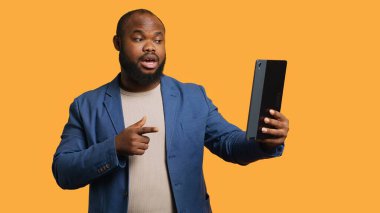 Telekonferans sırasında arkadaşlarıyla sohbet eden neşeli bir adam tablet, stüdyo arka planı kullanıyor. Mutlu insan çevrimiçi video görüşmesi sırasında arkadaşlarıyla eğleniyor, kamera A