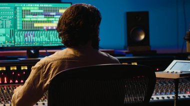 Pistleri düzenlemek ve işlemek için kontrol odasında çalışan ses teknisyeni, müzik endüstrisi sonrası prodüksiyon için bilgisayarda ses yazılımı kullanıyor. Yetenekli yapımcı karıştırma konsoluyla müzik yapıyor. Kamera A.