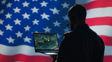 A.B.D. Hava Kuvvetleri harekat subayı cihazdaki izleme iletimini inceliyor, kontrol odasından yer askerlerine kulaklık kullanarak veri aktarıyor, ABD bayraklarında izole edilmiş, kamera A