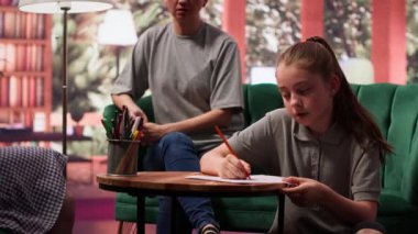 Genç kız, yaratıcı terapi seansının bir parçası olarak çizim yapıyor. Annesine ve terapistine danışmanlık, stres atmak ve duygusal yönetim için sanat eserlerini kullanmaya odaklanıyor. Kamera A.