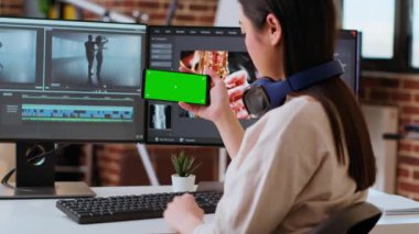 Evde çalışan Asyalı kadın editör yeşil ekran için çalışıyor, akıllı telefon ve video karıştırma yazılımı için çift monitör kullanıyor. Teknolojik aletlerle donatılmış yaratıcı çalışma alanı. Kamera B.