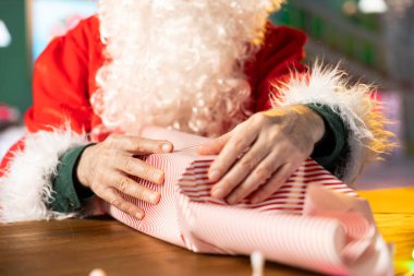 Noel Baba güzel paketlenmiş bir hediye kutusunu güzel ambalaj kağıdıyla süslüyor. Bayram ruhunu ışık ve süslemelerle yayıyor. Noel Baba, Kuzey Kutbu atölyesinde hediyeler hazırlıyor..