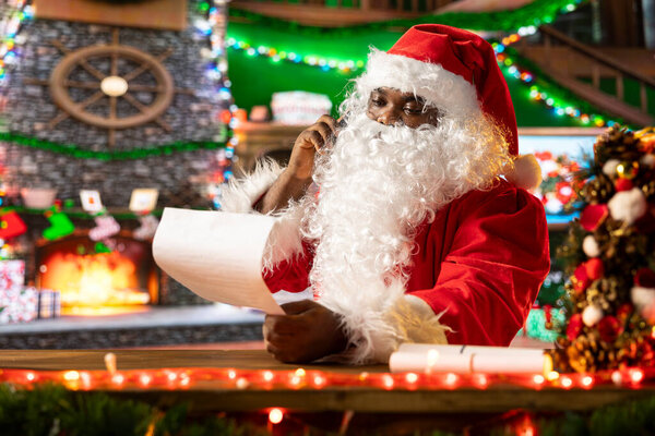 Santa Claus reading letters by the fire to spread the holiday spirit, chatting on a phone call. Traditional Christmas scene of festive joy captures the warmth and magic of the season.