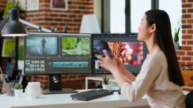 Asyalı film yapımcısı kadın kulaklık takıyor ve video yapımında çalışıyor, video klipleri karıştırıyor. Prodüksiyon sonrası renk değerlendirmesi için mükemmel bir yazılımla ofis kurulumu. Kamera B.