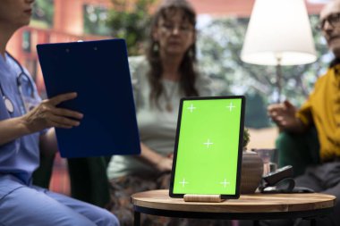 Yaşlı bir adam ve kadın evlerinde yeşil ekranlı bir tabletle hemşirelerle konuşuyor, eğlenceli bir sohbet ediyorlar ve rehberlik istiyorlar. Yaşlı çift iyi hissediyor, check-up ziyareti sırasında dinleniyorlar..