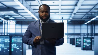 Modern veri merkezinde dizüstü bilgisayar üzerinde çalışan bilişim mühendisi, sunucu işlemleri, sistem bakımı ve siber güvenlik protokolleri, optimal performans ve veri bütünlüğü sağlanması, kamera A