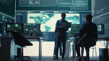 Ulusal veritabanı sunucularını inceledikten sonra hükümet hackerları siber saldırı simülasyonu yapıyor. Bilgi işleme uzmanları fidye yazılımına karşı veri ihlali önleme üzerinde çalışıyor. Kamera B.