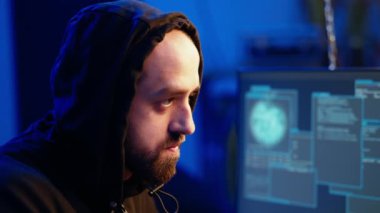 Hassas bağlantıları hedef alan, dijital cihazları tehlikeye atan ve değerli hassas verileri çalan kapüşonlu bir bilgisayar korsanı. Kötü adam duvar yazısıyla bodrumu boyuyor, kamera yakın plan.