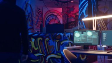 Hacker yeraltı üssüne geliyor, Grafiti çizimleriyle endüstriyel depodaki sprey kutulara bakıyor. Siber suçlu hackleme işlemini bekliyor, suç cennetindeki boya kutularına bakıyor, kamera B