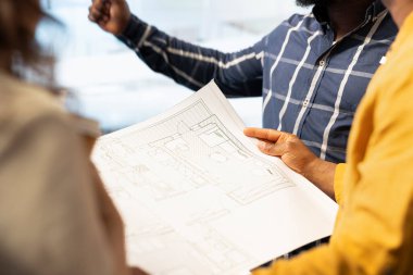 Mimari planlarını değerlendiren bir işletme ekibi, emlak yatırım anlaşmasını göz önünde bulundurarak, yüksek sınıf ofis alanının planlarını değerlendiriyor. Kiralama anlaşması için emlakçıyla pazarlık eden profesyoneller. Kapat..