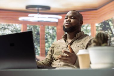 Evde dizüstü bilgisayardaki video görüşmesine katılan serbest çalışan bir adam online konferans ağındaki yatırımcılarla tartışıyor. Geliştirme için işletme işlemleri uzaktan yönetiliyor.