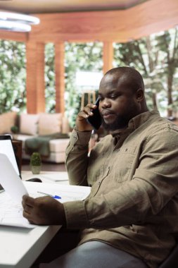 Girişimci ofis planı fikirlerini tasarımcılarla telefonda paylaşıyor, yeni yaratıcı çalışma alanı için bir bina yenilemesi planlıyor. Modern bir düzen için mimari planlar kullanılıyor..