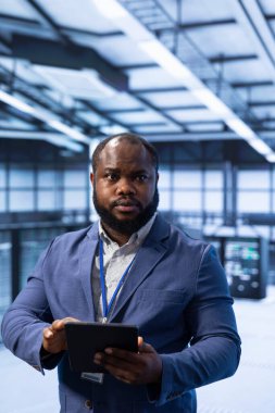 Technician in server hub workplace installing newly ordered storage unit, checking parameters with tablet. IT expert in data center holding device, replacing storage mainframes components clipart