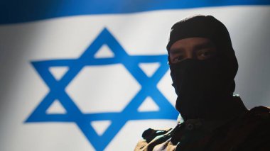 Mossad kılık değiştirmiş, maskeli bir casus İsrail bayrağı önünde gururla duruyor ve ülkesine hizmet etmekten gurur duyuyor. İsrail gizli ajanı, savaş kontrol odasında. Ülkeyi temsil ediyor.