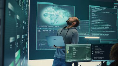 Siber savunma uzmanı, siber operasyonlara ve dijital güvenliğe odaklanan büyük bir ekrandaki verileri inceliyor. Hacker siber suç faaliyetlerine karşı koruma sağlıyor. Kamera B.