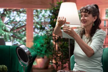 Son sınıf öğrencisi kadın aynaya bakıyor ve yüzüne yaşlanma önleyici krem sürüyor cildini korumak için yenileyici ürünler kullanıyor. Emekli adam serum ve losyonla şımartma rutini yapıyor..